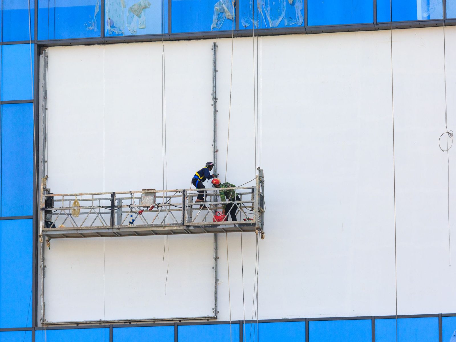 Two workers on a suspended platform at a white building facade